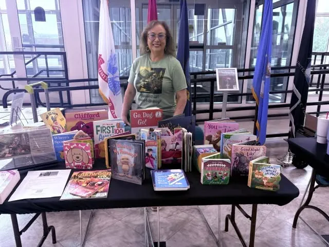 A volunteer in an Appalachian Books & Blessings shirt stands behind a table covered with children's books.